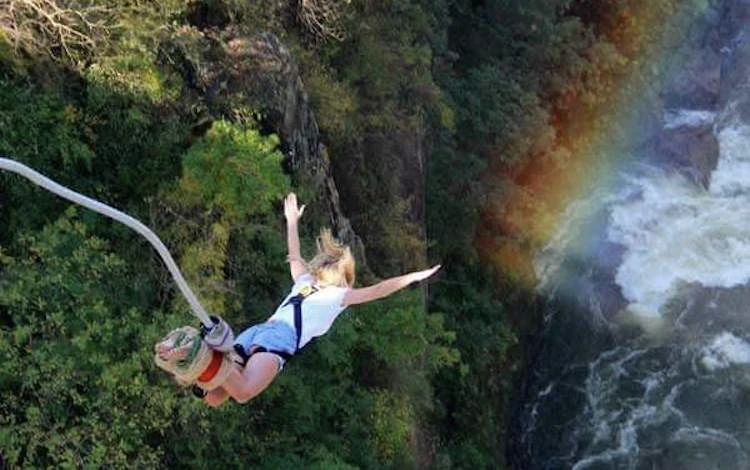 Women in white shirt and blue shorts bungee jumping from bridge connecting Zambia and Zimbabwe