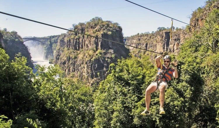 Man zip lining through the air above the Zambezi River while checking out the spectacular view in Zimbabwe.