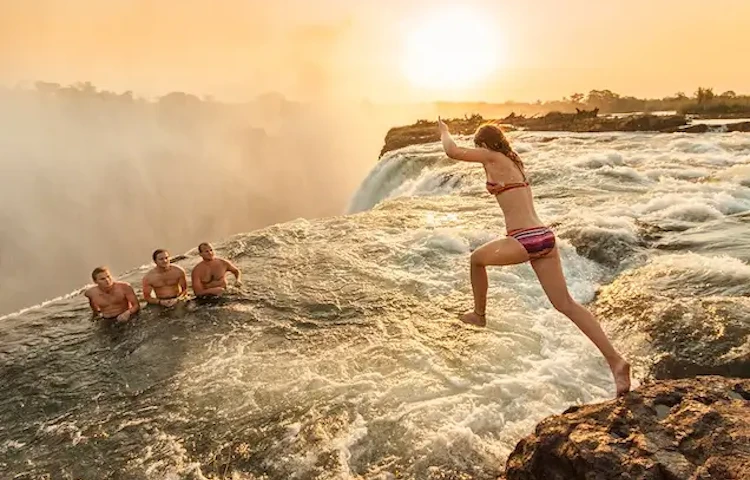 3 men on the edge of Devil's pool in Zambia, while girl leaps into the pool from a rock!